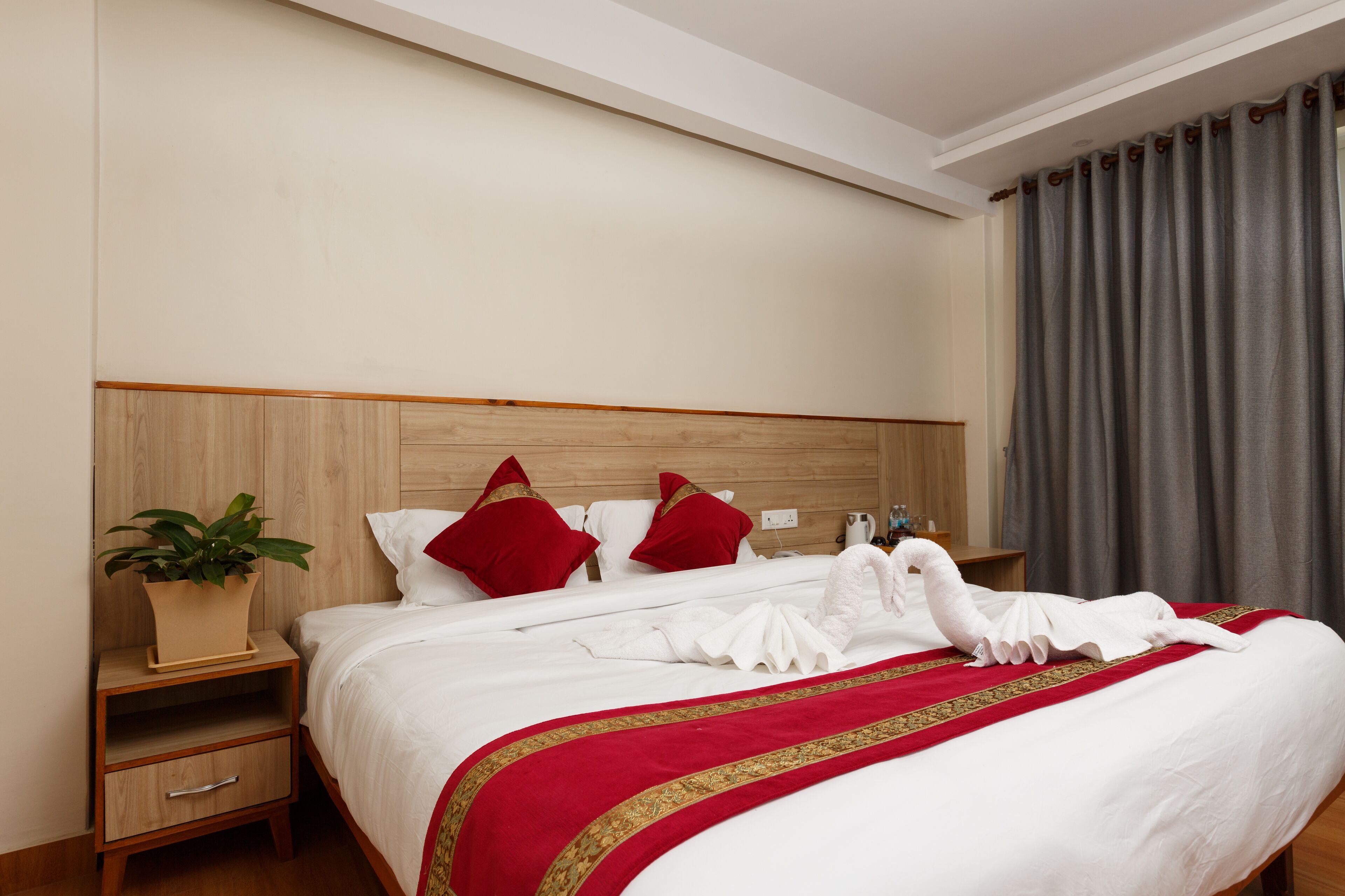 A neatly made bed with a red and gold bedspread, white pillows, and a swan-shaped towel arrangement.