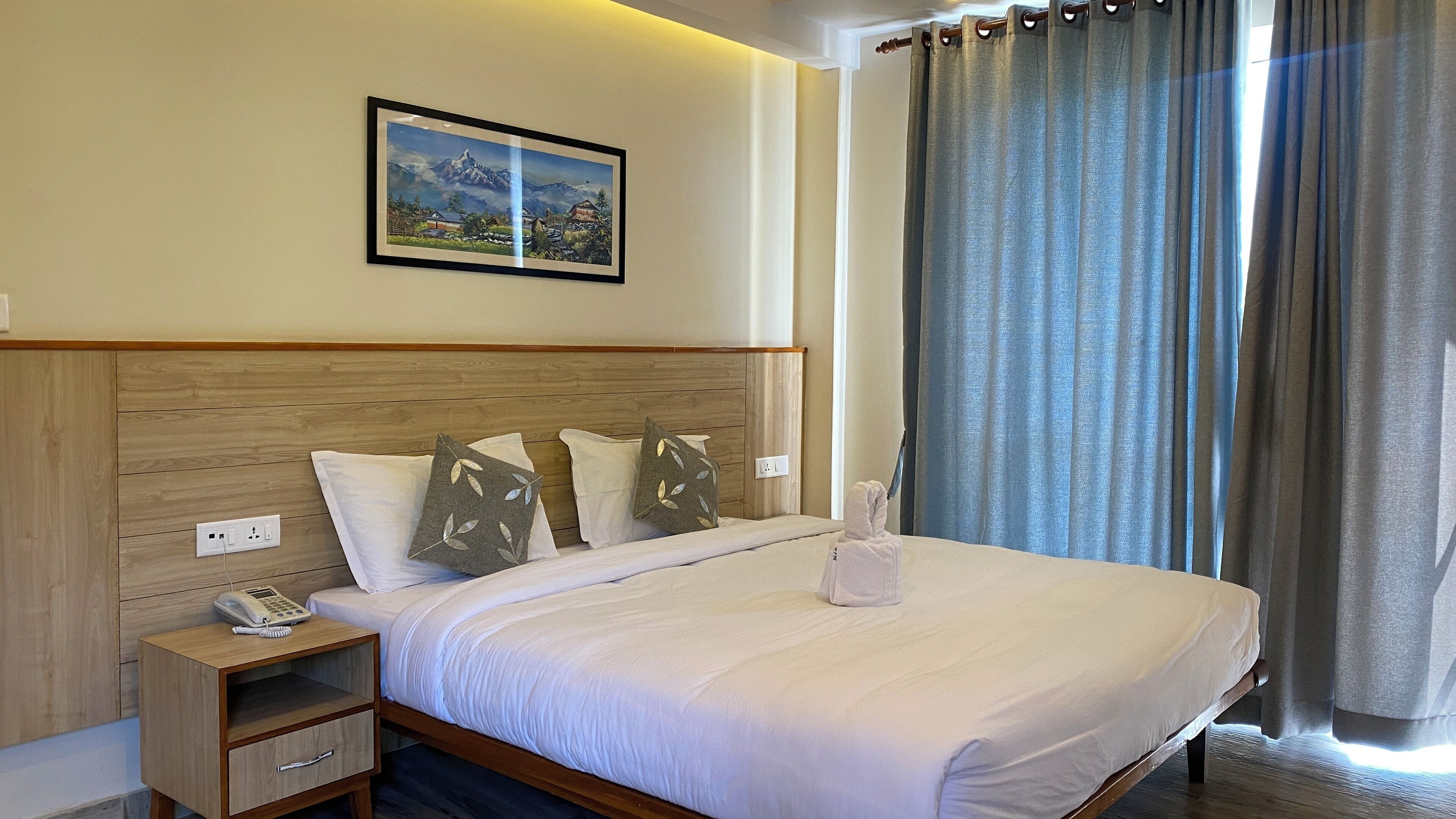 A hotel room with a wooden headboard, a bedside table with a phone, a neatly made bed with white linens, and a painting above the bed.