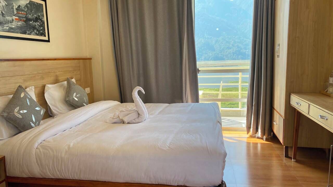 A hotel room with a bed, a desk, and a view of a mountainous landscape.