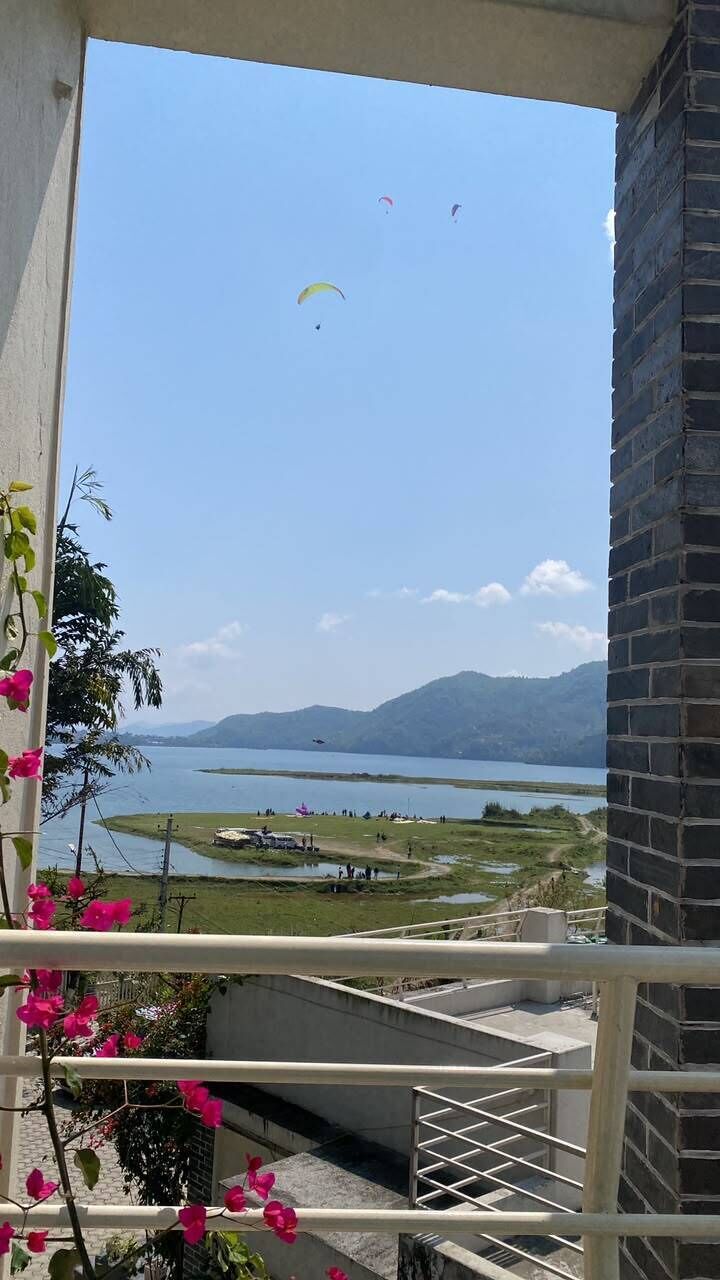 A balcony with a view of a lake and mountains, a brick wall, and pink flowers.