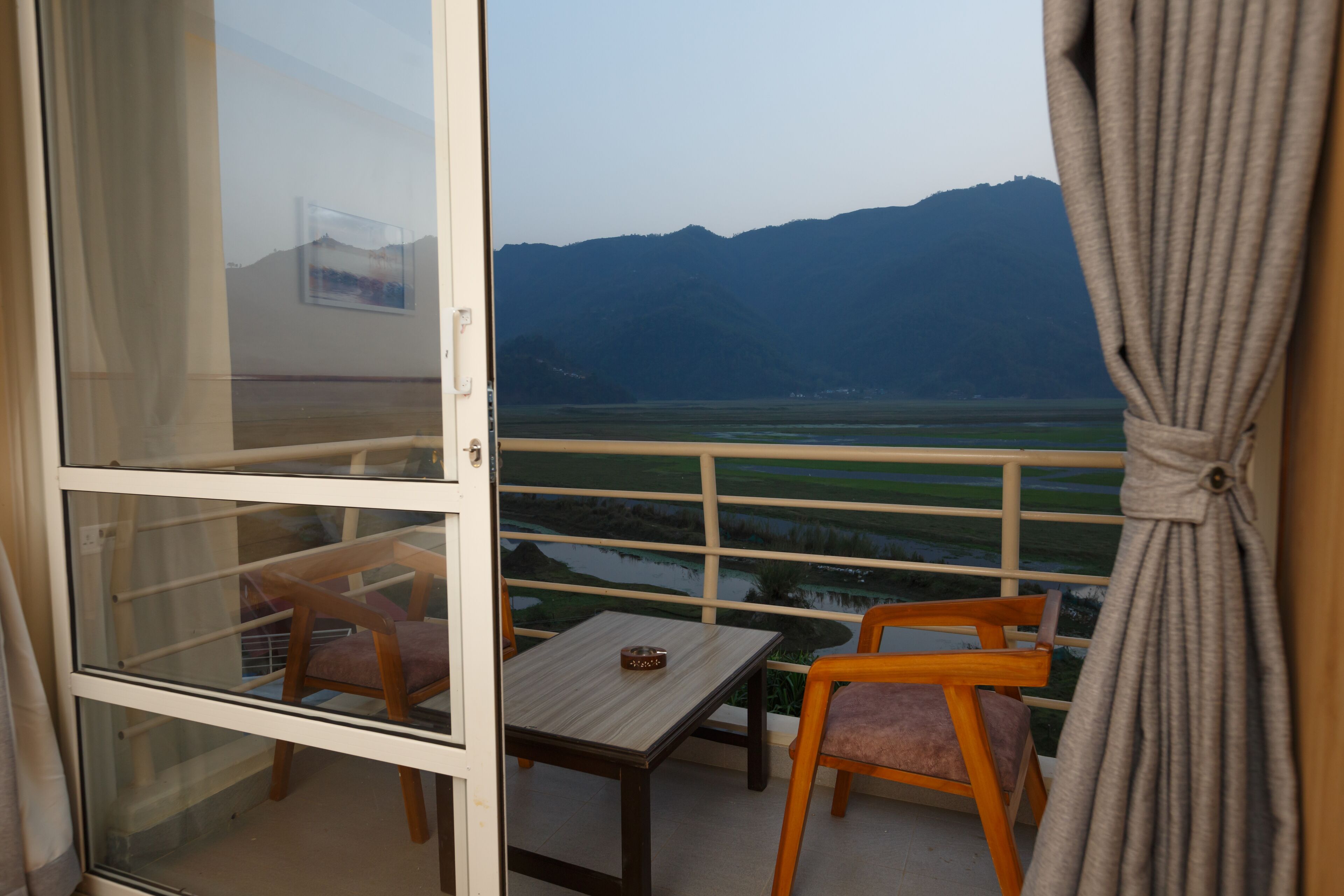 A balcony with a table and two chairs, overlooking a scenic view of mountains and a body of water.