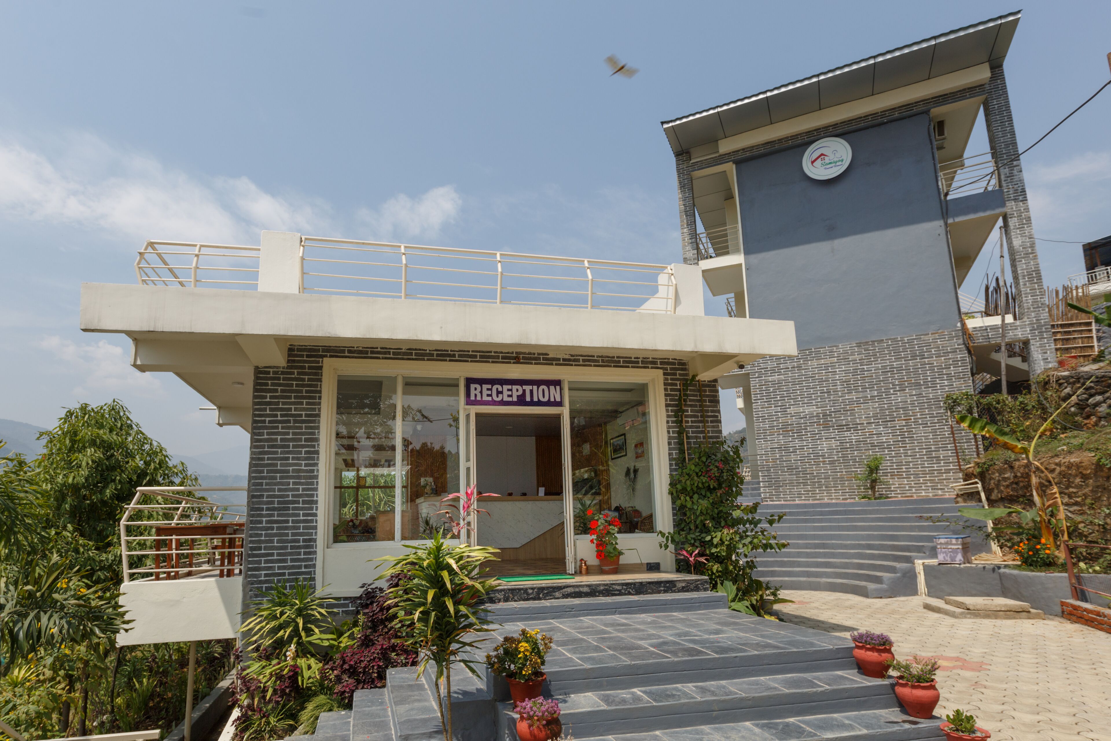 A reception area with a sign, potted plants, and a staircase leading to a building.