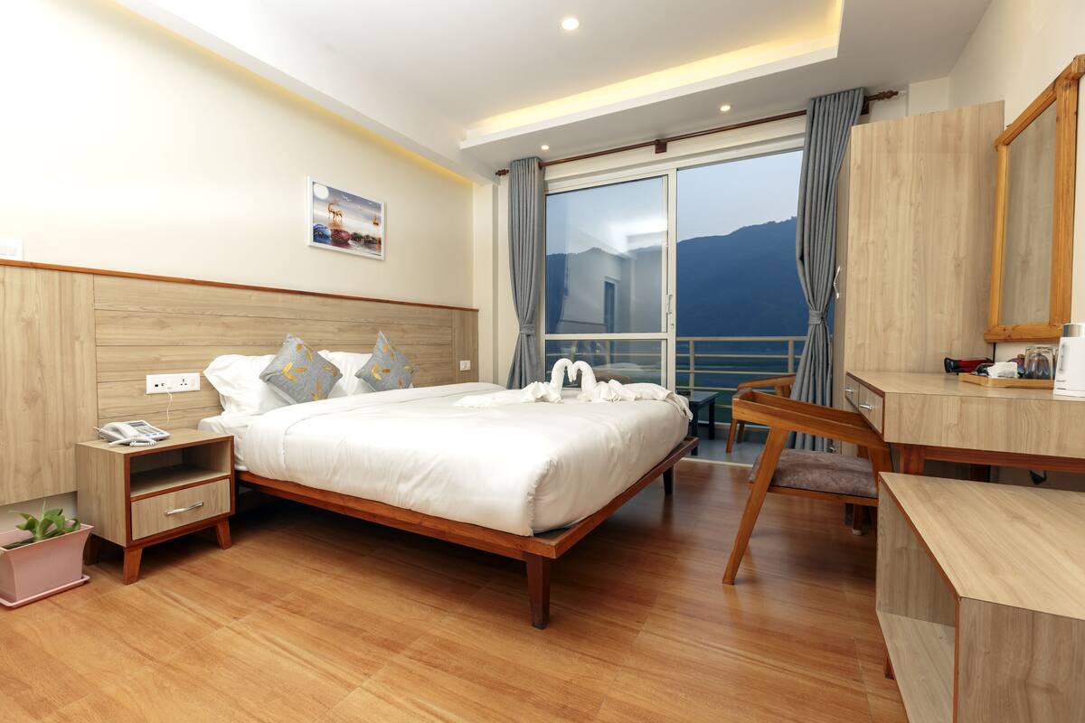 A modern hotel room with a wooden bed, a desk, and a view of the mountains.