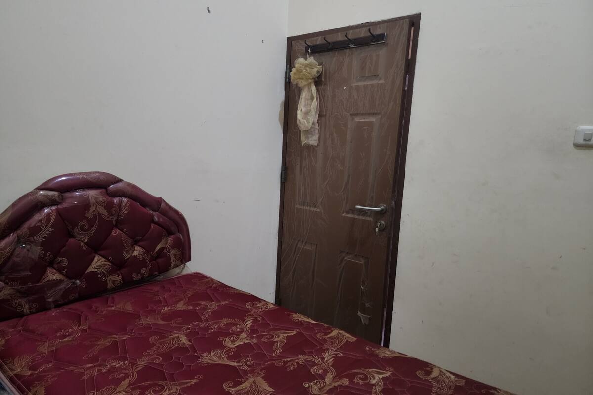 A bedroom with a bed, a wooden door, and a wall-mounted light switch.