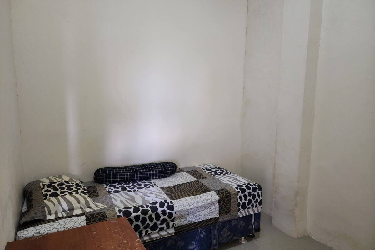 A corner of a room with a bed covered in a patchwork quilt and a blue sofa with a patterned cushion.