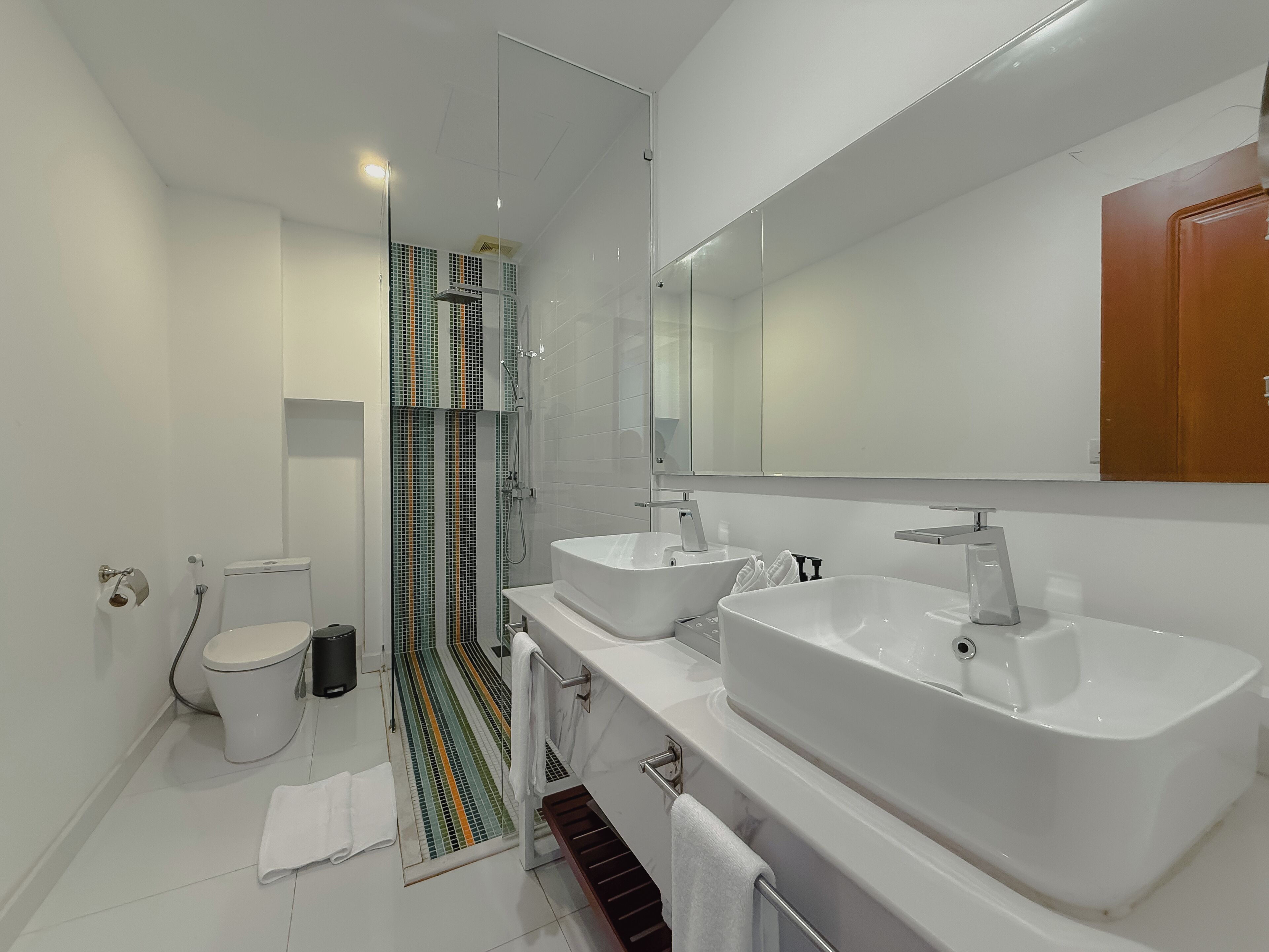 A modern bathroom with a toilet, bidet, and a shower with a glass door. There are two sinks with mirrors above them.