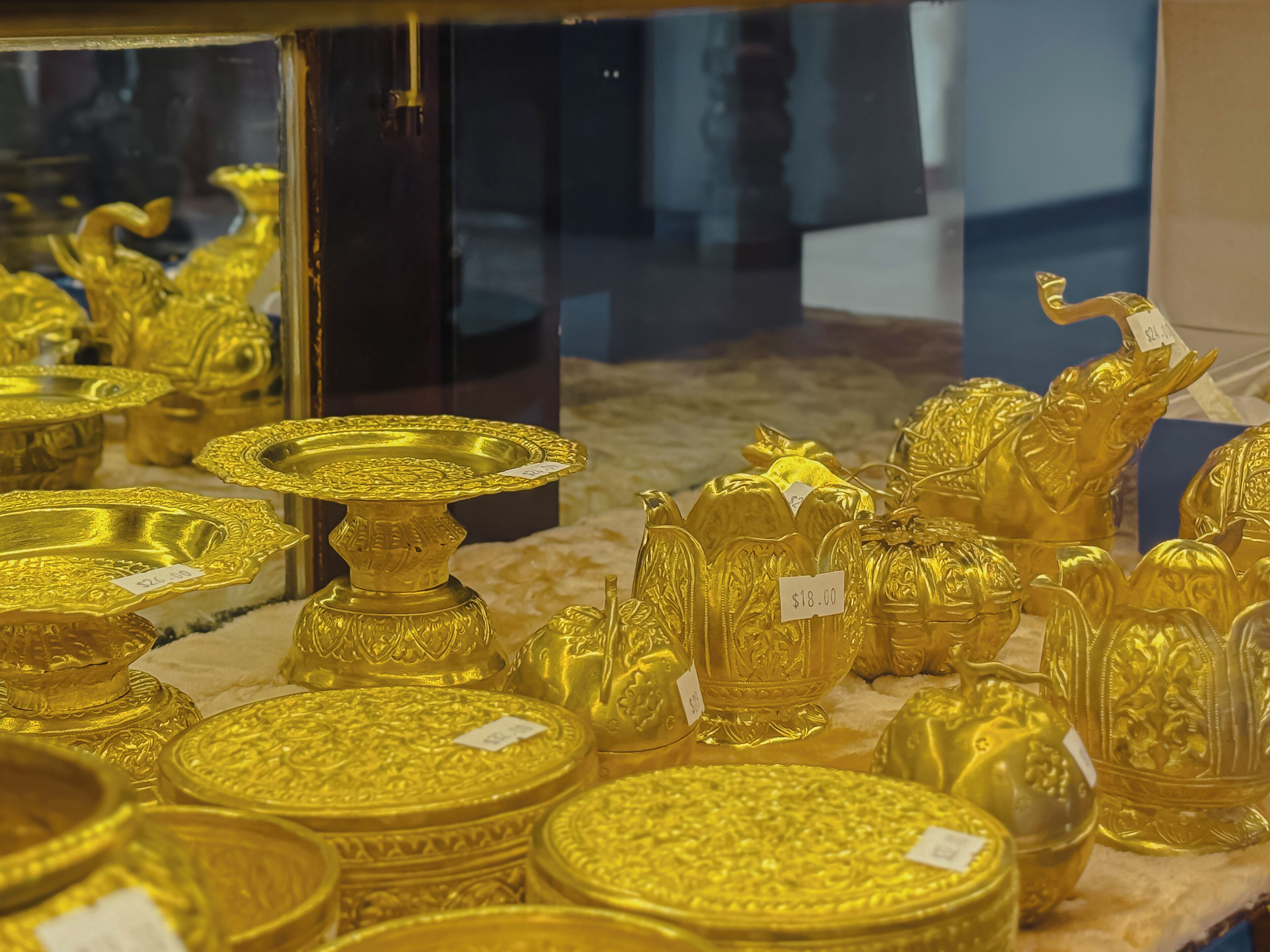 A display of various gold items, including plates, vases, and figurines, with price tags visible.