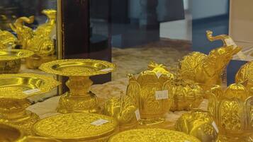 A display of various gold items, including plates, vases, and figurines, with price tags visible.