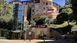 Un hôtel doté d’une entrée moderne en verre, d’une enseigne portant le nom « Tivoli » et d’un jardin bien entretenu.