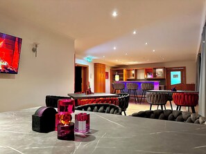Relax in a spacious room with a large flat-screen TV, comfortable seating area, and bar with stools.