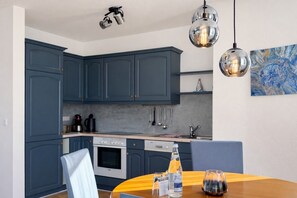 A modern kitchen with dark blue cabinets, a stainless steel range, and a dining area with a wooden table and chairs.