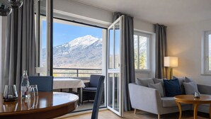 Une chambre d’hôtel avec vue sur la montagne, un coin repas avec une table et des chaises, un canapé et une lampe.