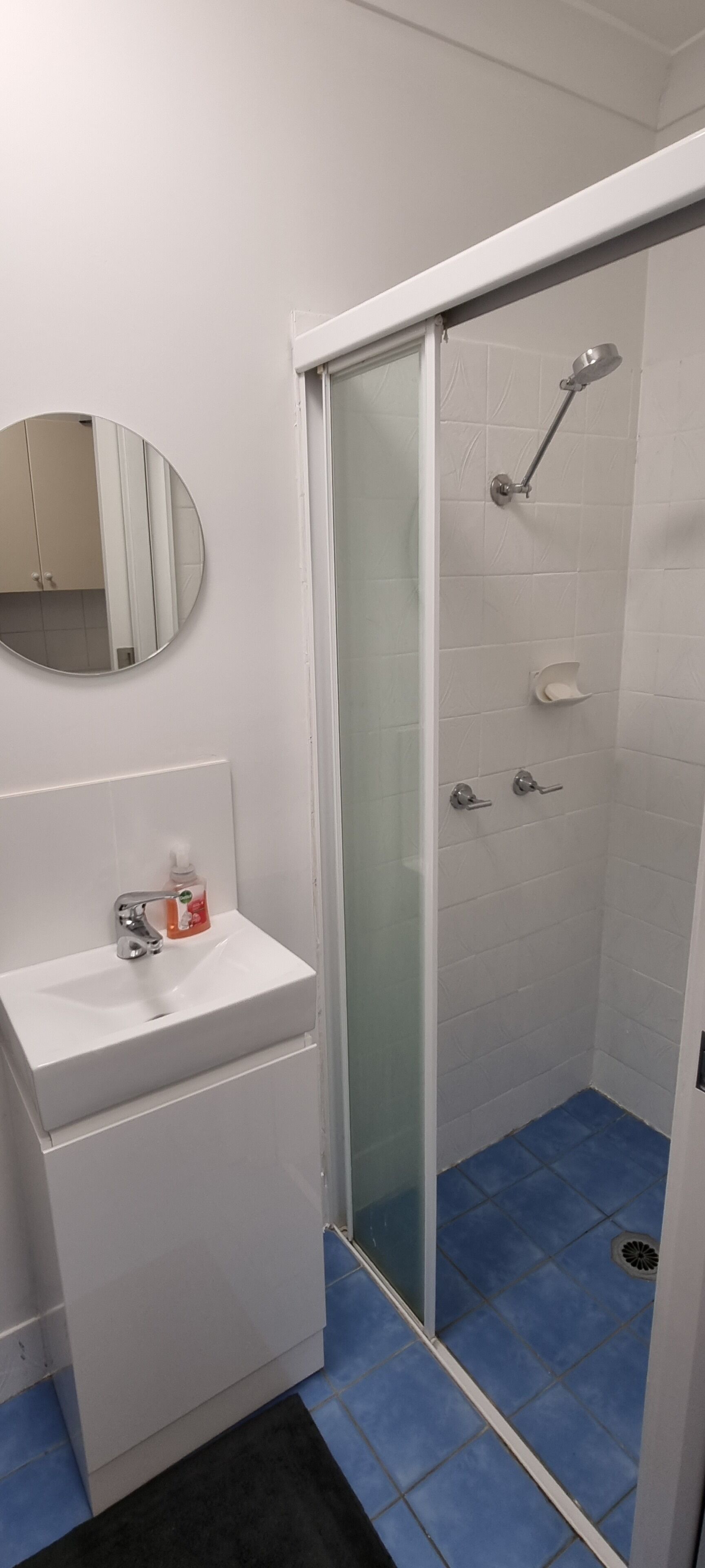 Een badkamer met een witte wastafel, een spiegel, een douche met een glazen deur en blauw betegelde vloer.