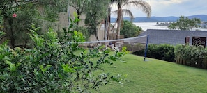 Zona verde con una red de voleibol, árboles y vistas de un cuerpo de agua y colinas al fondo.