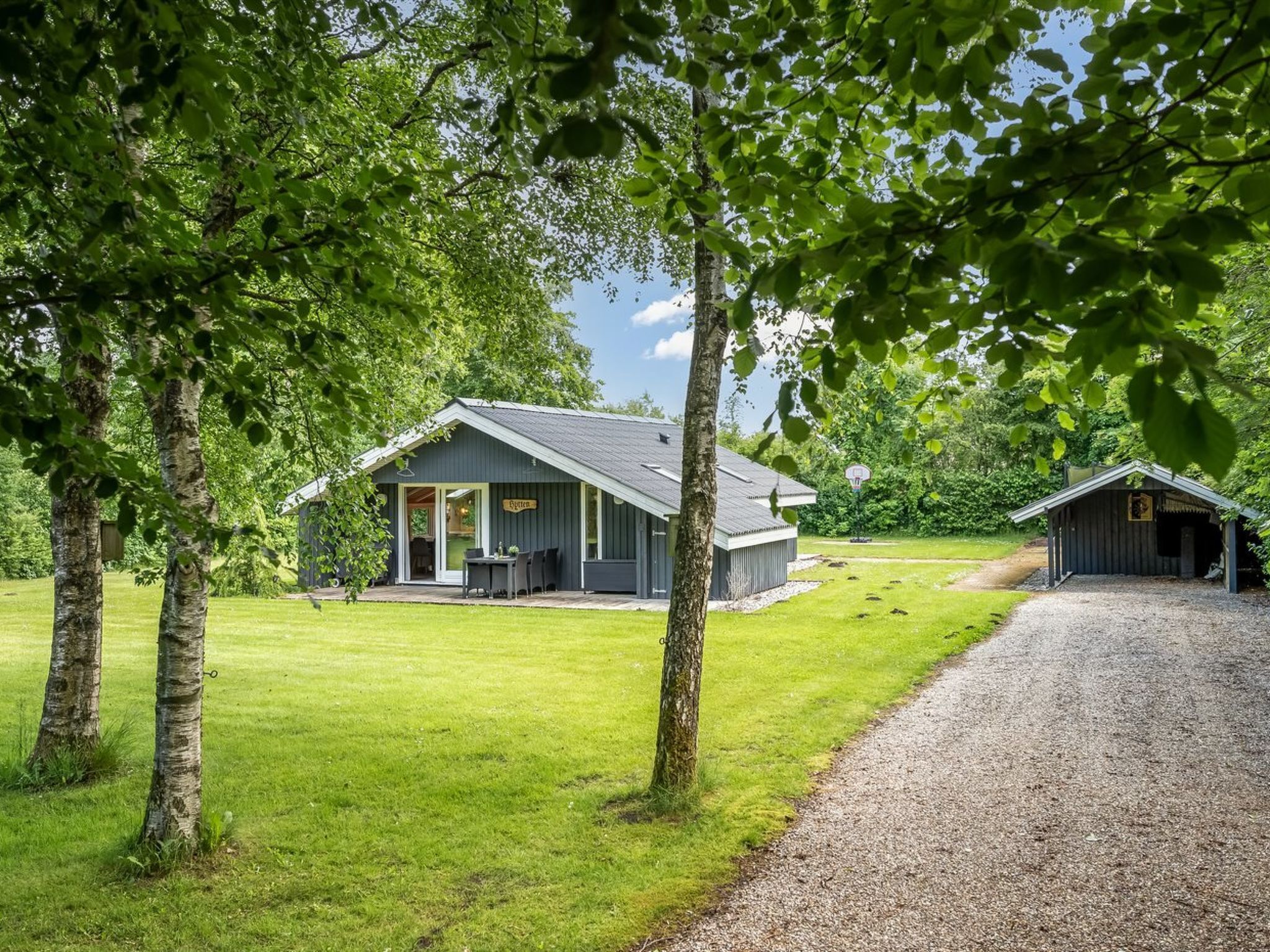 Tunnelmallinen mökki, jossa on kuisti, koripalloteline ja soralla päällystetty polku.