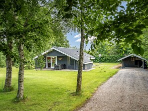 A rustic cabin with a porch, a basketball hoop, and a gravel path.