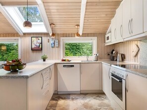 A modern kitchen with wooden cabinets, a dishwasher, an oven, and a window with a view of greenery.