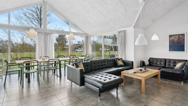 A spacious living area with a large window, a black leather sofa, a wooden coffee table, and a dining area with green chairs and a table. - "Sada" - 12km from the sea by Interhome (Oksbøl)