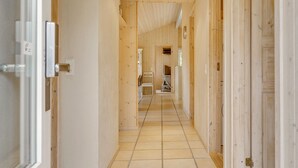 Ein schmaler Korridor mit Holzwänden und Fliesenboden, der zu einem Zimmer mit Bett und Stuhl führt.
