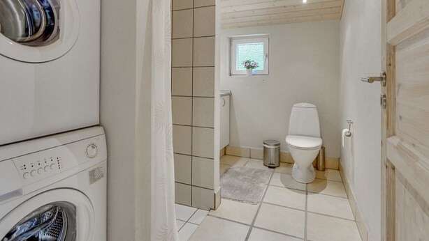 Ein kleines Badezimmer mit Waschmaschine, Toilette und einem Fenster mit Pflanze.