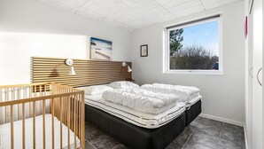 A bedroom with a crib, a bed with two pillows, a headboard, a window with a view, and a picture on the wall. - "Talida" - 12km from the sea by Interhome (Oksbøl)
