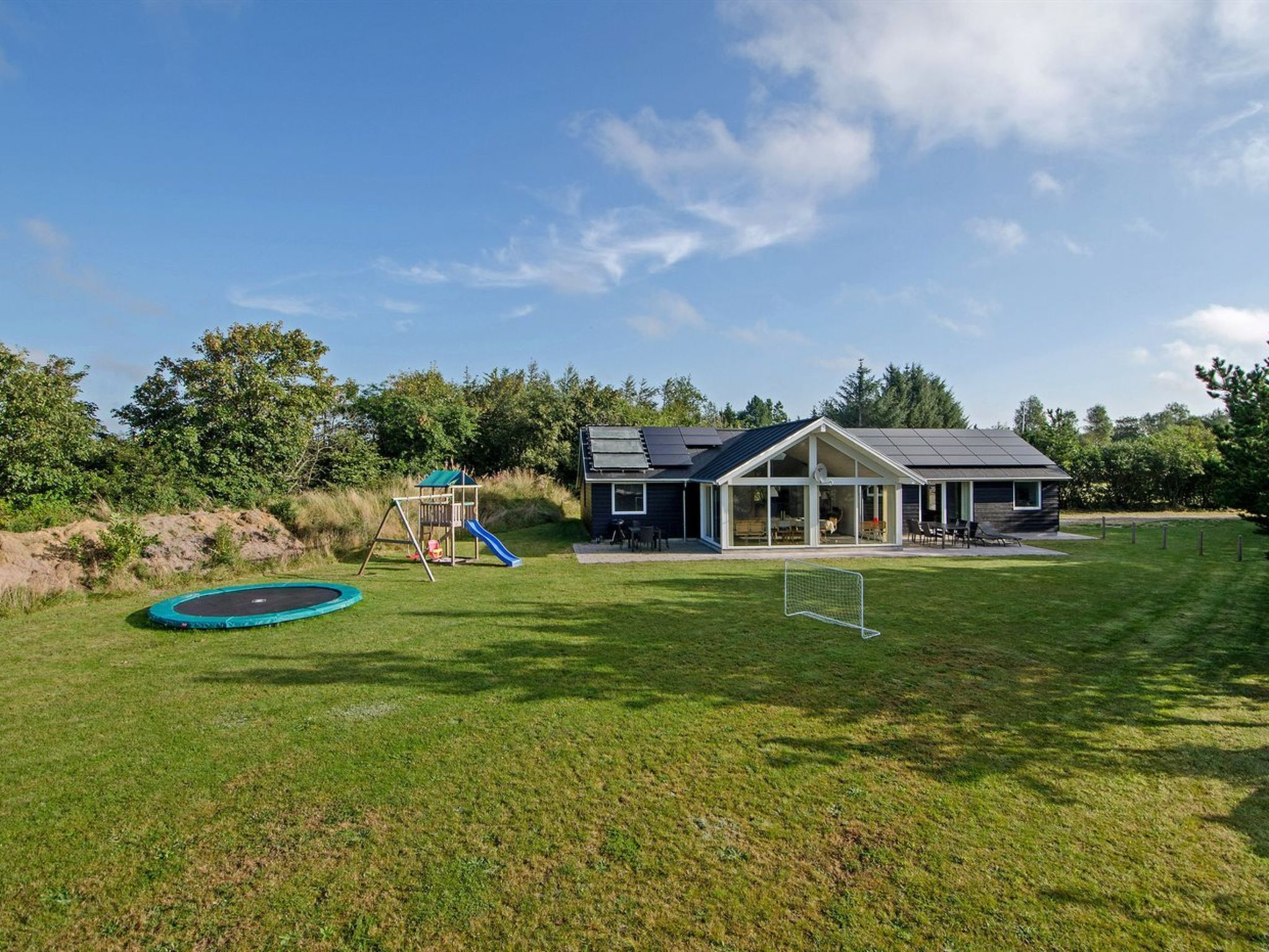 Ein Haus mit einem großen Garten, der ein Trampolin, ein Spielhaus und ein Fußballtor beinhaltet.