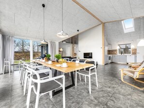 Un comedor amplio con una larga mesa de madera y sillas blancas, una cocina con electrodomésticos modernos y un ventanal con vistas al exterior.