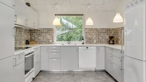 A modern kitchen with white cabinets, a built-in oven, a dishwasher, and a window with a view of greenery. - "Talida" - 12km from the sea by Interhome (Oksbøl)