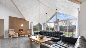 A spacious living area with a high ceiling, a black leather sofa, a wooden coffee table, and a dining table. - "Talida" - 12km from the sea by Interhome (Oksbøl)