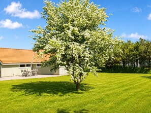 A tree-lined lawn with a building featuring a tiled roof and a patio area.