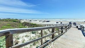 Une promenade en bois mène à une plage où des véhicules sont stationnés le long du bord.