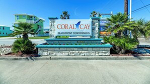 Une enseigne indiquant l’emplacement des appartements de Coral Cay, situés en bord de mer, offrant une vue dégagée sur les bâtiments environnants et les palmiers.