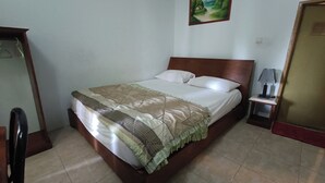 A neatly made bed with a patterned bedspread and pillows, a small bedside table with a lamp, and a painting on the wall. - Hotel O Cprc Inn Serpong (Cisauk)
