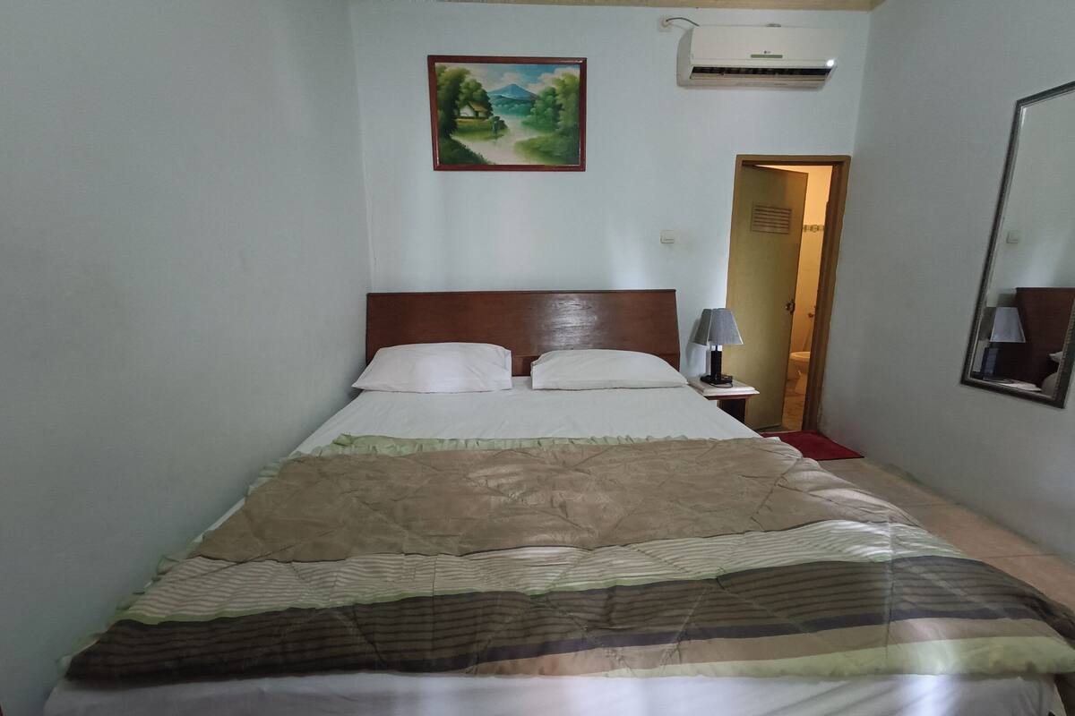 A neatly made bed with a striped blanket, a wooden headboard, and a framed landscape painting on the wall.