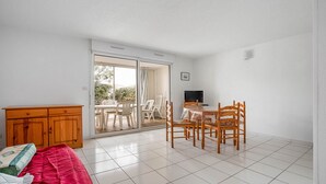A room with a sliding glass door leading to an outdoor area, a wooden cabinet, a dining table with chairs, and a television. - Large terrace, Appt 4 pers - near the beach (Agde)