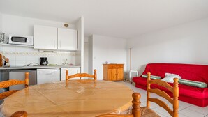 A compact living space with a dining table, chairs, a red sofa, a kitchen area with a microwave, and a radiator. - Large terrace, Appt 4 pers - near the beach (Agde)