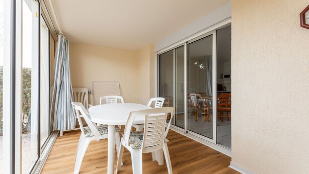 A balcony with a table and chairs, a sliding glass door, and a view of the interior. - Large terrace, Appt 4 pers - near the beach (Agde)