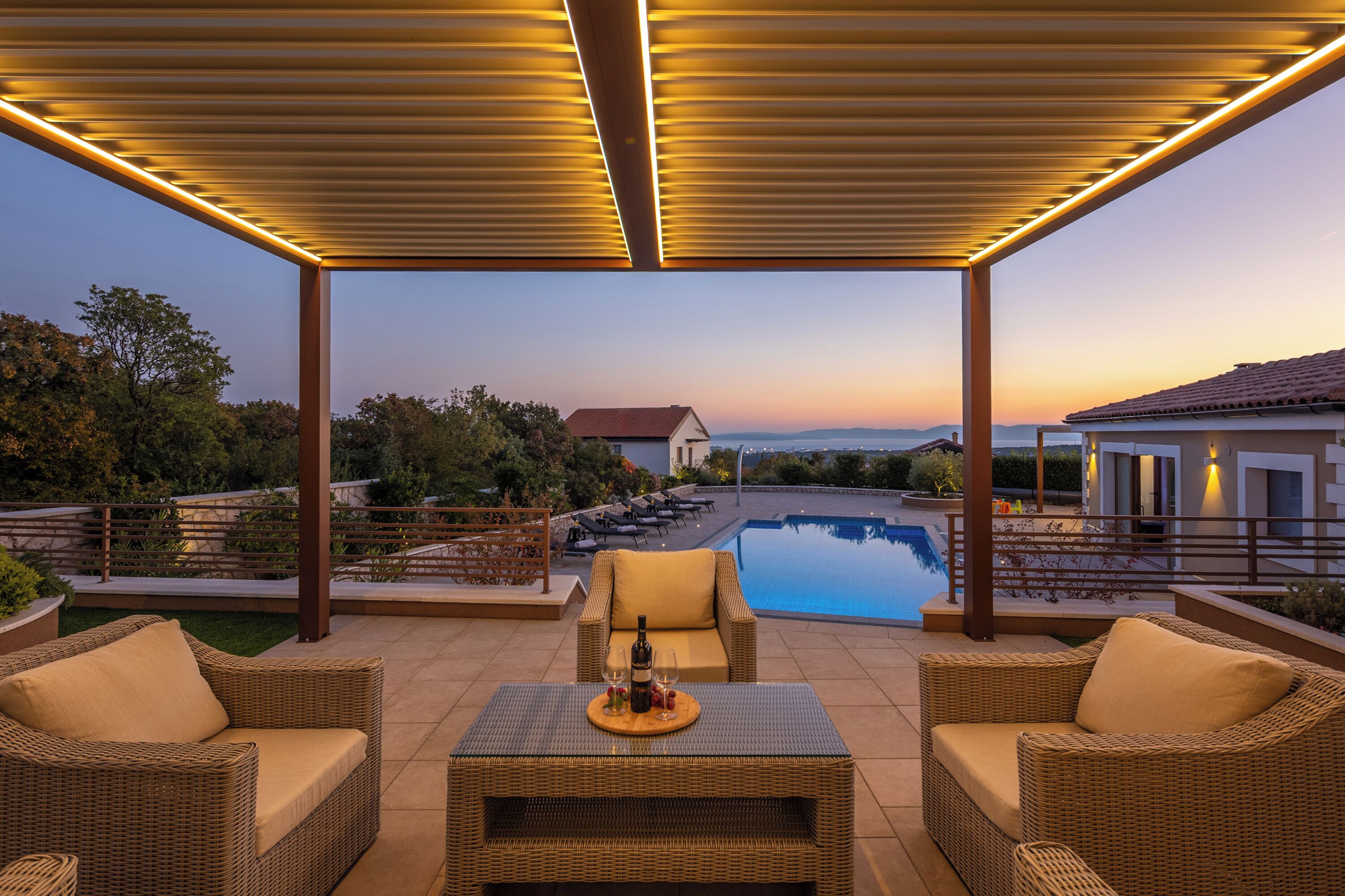A covered outdoor area with a pool, wicker furniture, and a view of the landscape.