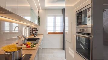 A modern kitchen with a built-in oven, a stainless steel refrigerator, and a window with curtains.