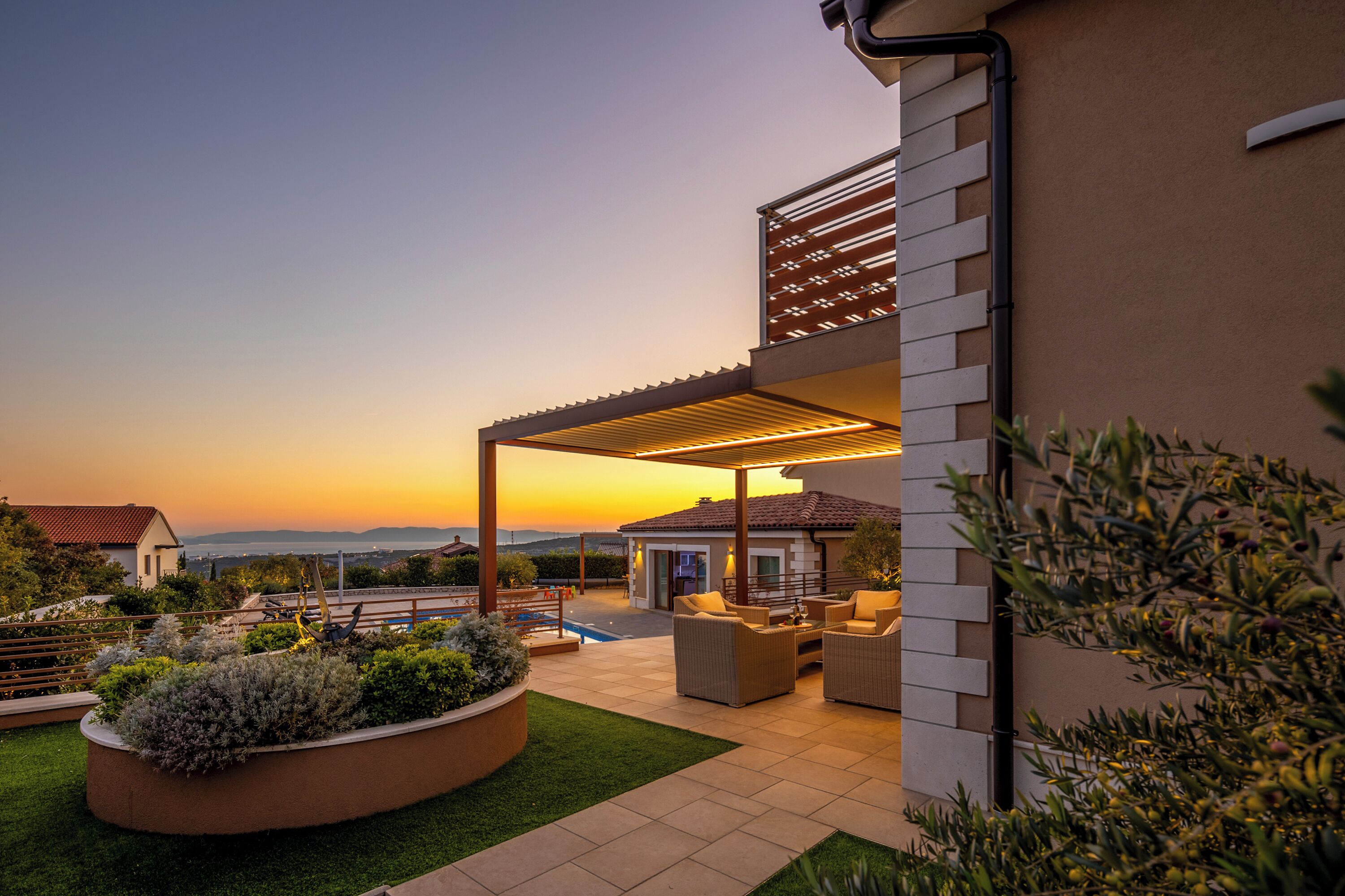 A covered outdoor patio with seating, a swimming pool, and a view of the sunset.