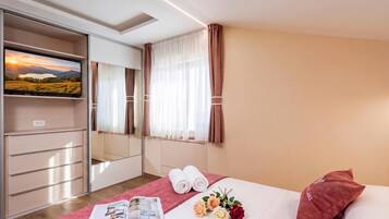 Una habitación de hotel con cama, televisión, armario y ventana con cortinas.