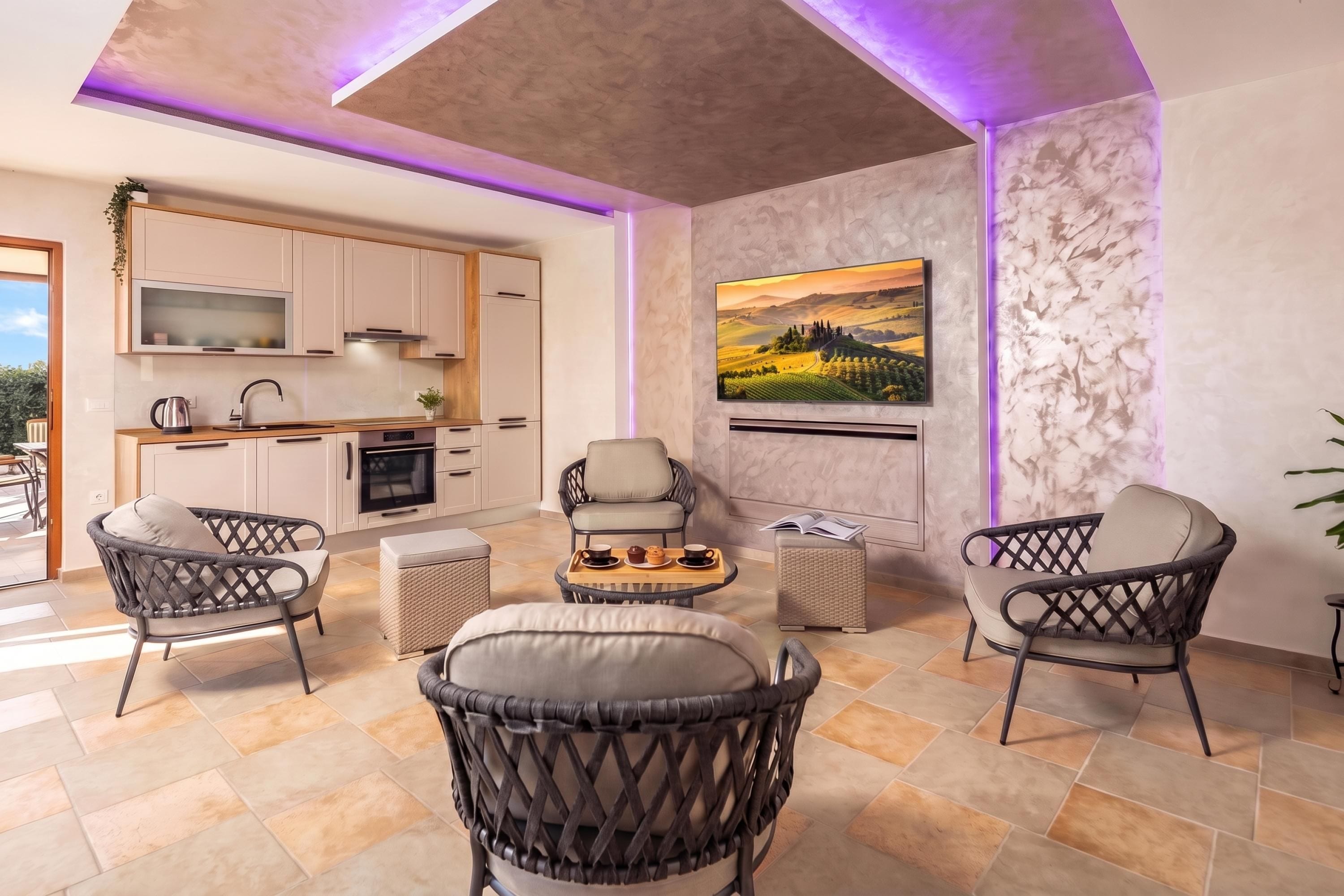Una sala de estar moderna con muebles de mimbre, una cocina al fondo y un cuadro de paisaje grande en la pared.