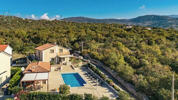 Una villa con piscina, rodeada de exuberante vegetación y colinas.