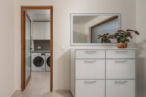 A modern laundry room with a washing machine and dryer, a white cabinet with drawers, and a mirror above the cabinet. - Villa Vilani Spa & Pool (Bakar)