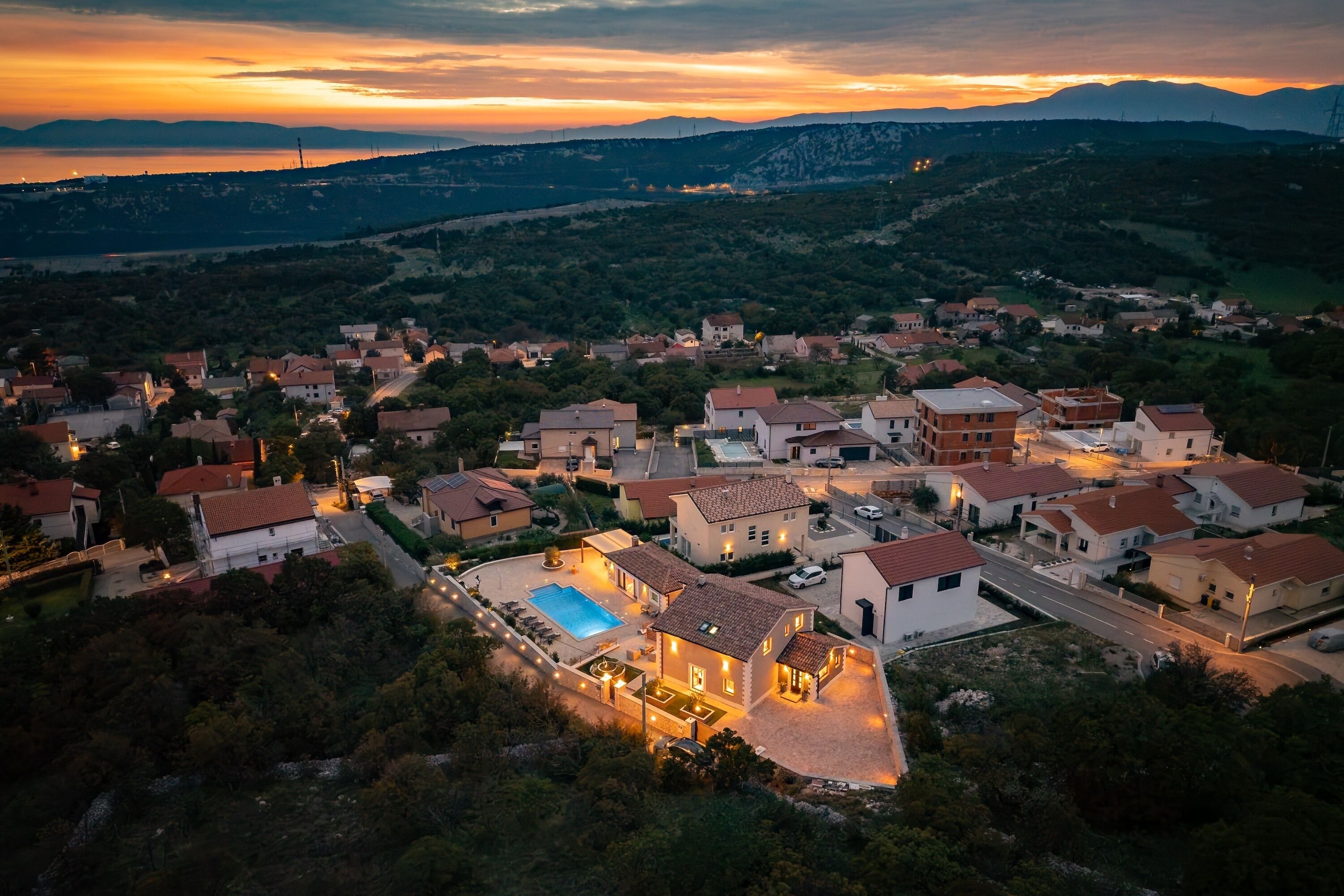A residential area with houses, a swimming pool, and a hilly landscape in the background.