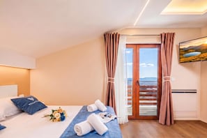 A hotel room with a bed, a blue bedspread, a bouquet of flowers, rolled towels, and a painting of a landscape.