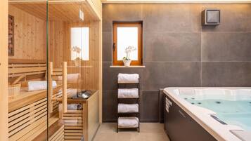 Una sala de sauna con bancos de madera, una puerta de cristal, una ventana con una planta y una bañera de hidromasaje.