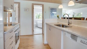 Een moderne keuken met houten vloeren, witte kasten, een ingebouwde oven en een groot keukenblok met een spoelbak.