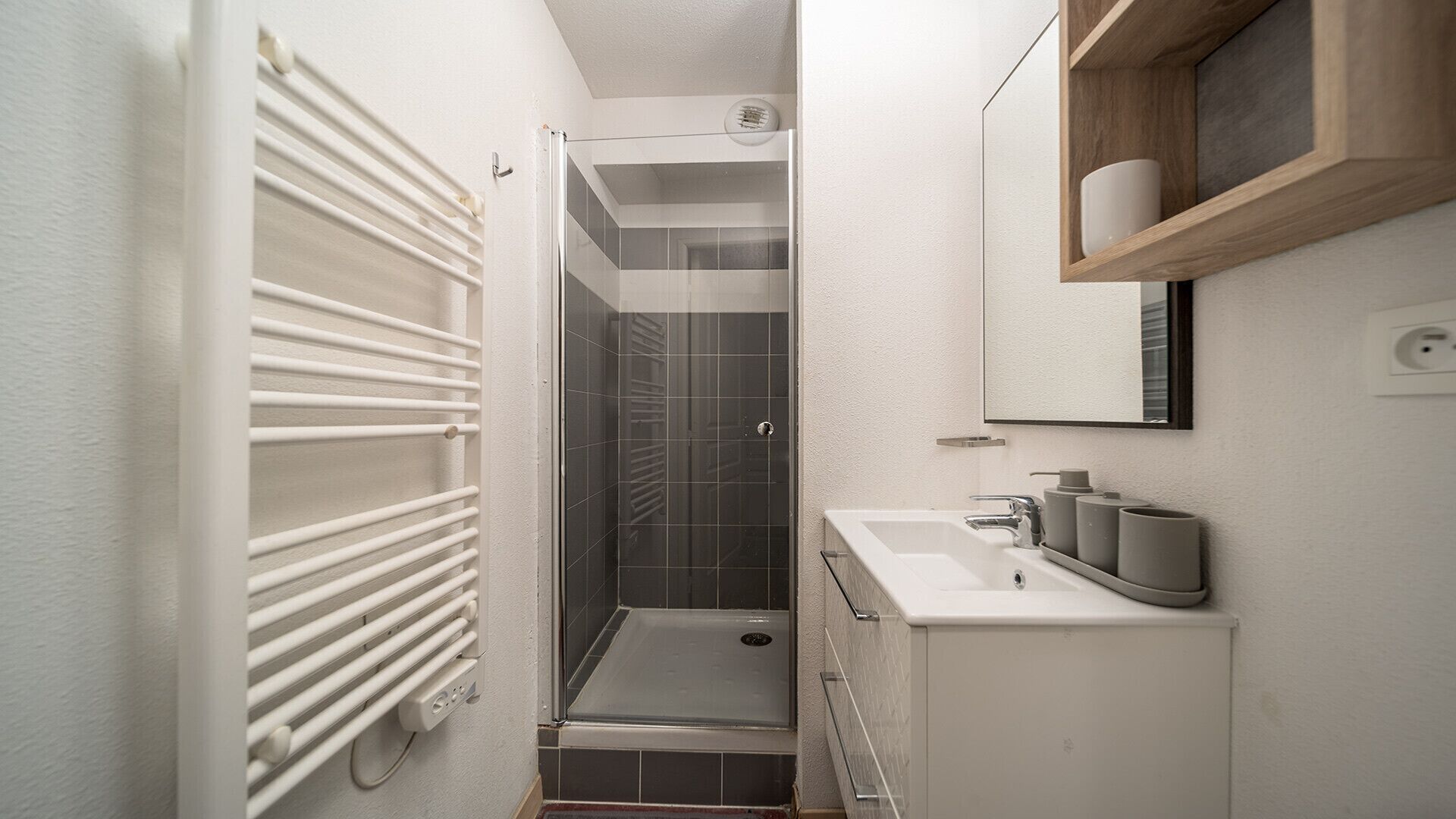 A narrow bathroom with a shower, a white sink, and a mirror above it.