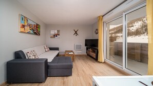 A modern living room with a sofa, a television, and a large window with a view of a snowy landscape.